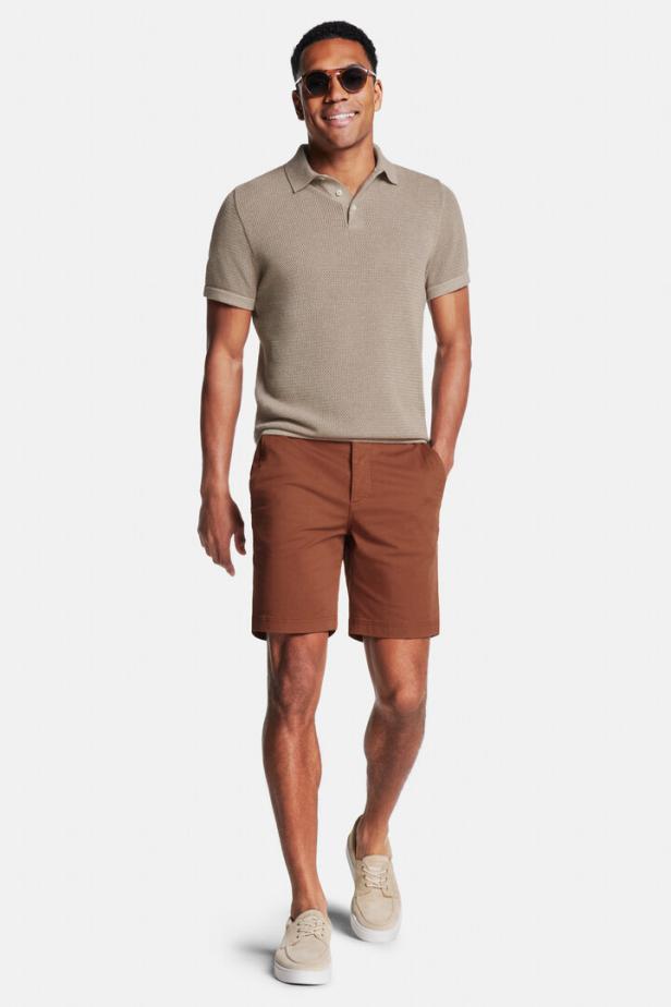 Ein Mann mit Sonnenbrille trägt ein beiges Poloshirt und braune Shorts.