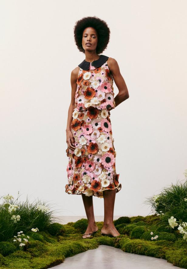 Eine Frau trägt ein zweiteiliges Blumenkleid mit schwarzem Kragen vor einem hellen Hintergrund.