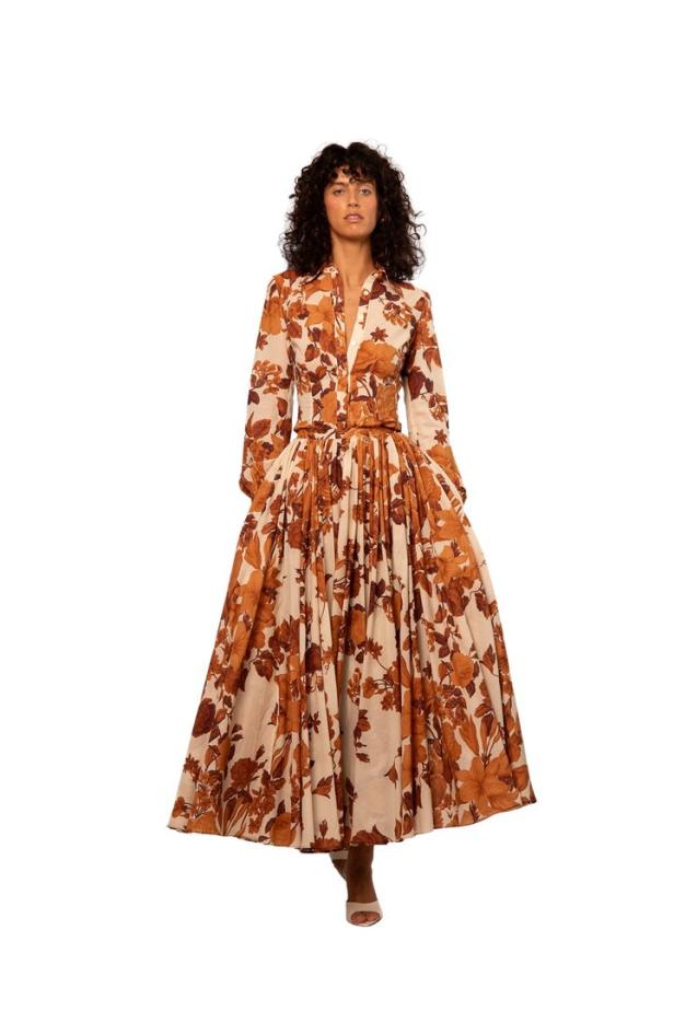 Frau mit lockigen Haaren trägt ein langes, beiges Kleid mit braunem Blumenmuster und Taillengürtel.