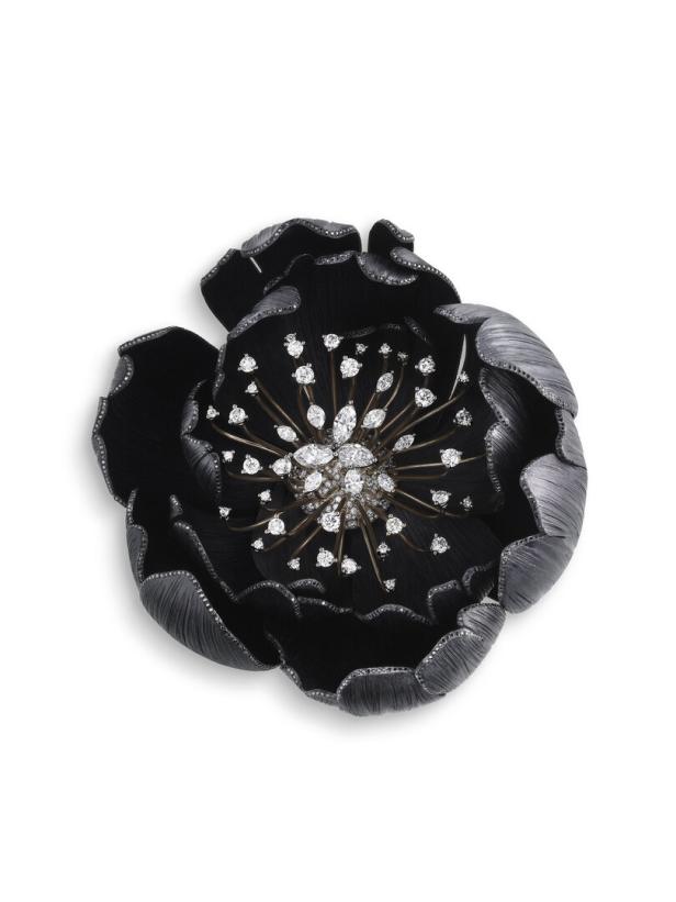 Eine schwarze, blütenförmige Brosche ist mit Diamanten im Zentrum und auf den Blütenblättern besetzt.