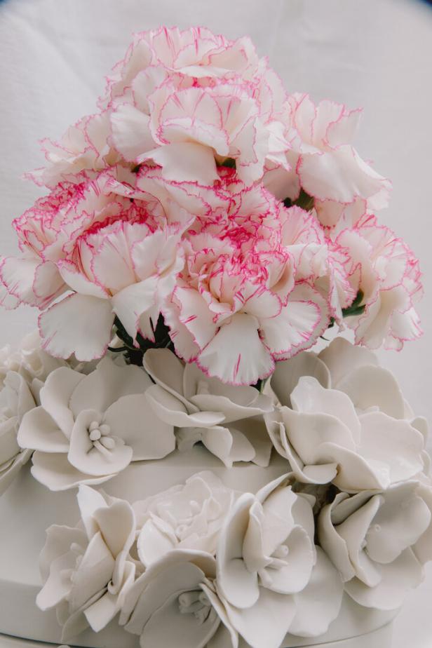 Weiße Nelken mit rosa Rand stehen auf einem weißen Behälter mit Blumenrelief.