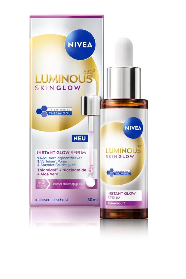 Eine Nivea Luminous Skin Glow Serum-Flasche und die zugehörige Verpackung stehen auf einer reflektierenden Oberfläche.