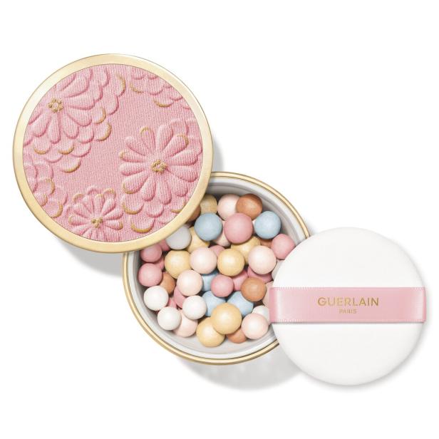 Runde Dose mit pastellfarbenen Puderperlen, daneben eine weiße Puderquaste mit rosa Band und goldener Aufschrift.