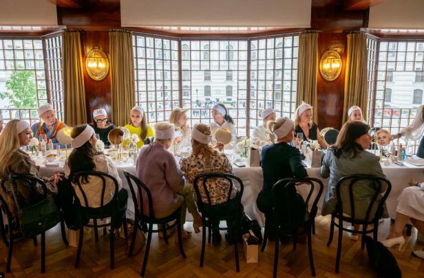 Teilnehmerinnen des exklusiven Helena Rubinstein Hautpflege-Workshops sitzen mit Spiegeln und Stirnbändern an einem festlich gedeckten Tisch im Looshaus am Michaelerplatz.