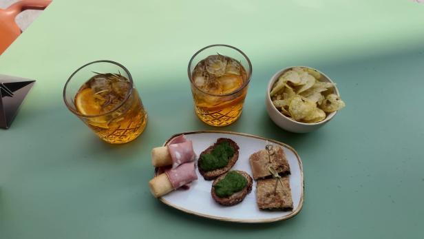 Zwei Getränke mit Eis, Chips und eine Platte mit Canapés stehen auf einem Tisch.