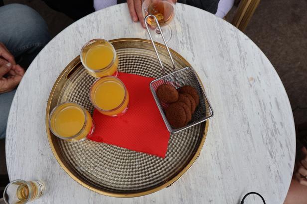 Auf einem Tisch stehen drei Gläser Orangensaft und ein Korb mit Keksen auf einem goldenen Tablett.