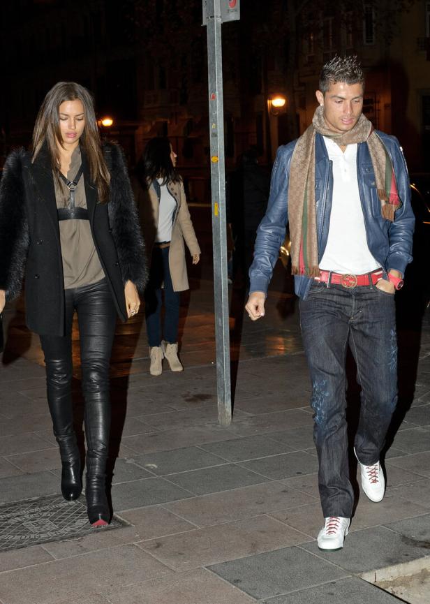 Cristiano Ronaldo und Irina Shayk gehen abends modisch gekleidet auf einem Gehweg in der Stadt spazieren. er trägt Jeans, eine blaue Lederjacke und eine karierten Gucci-Schal.