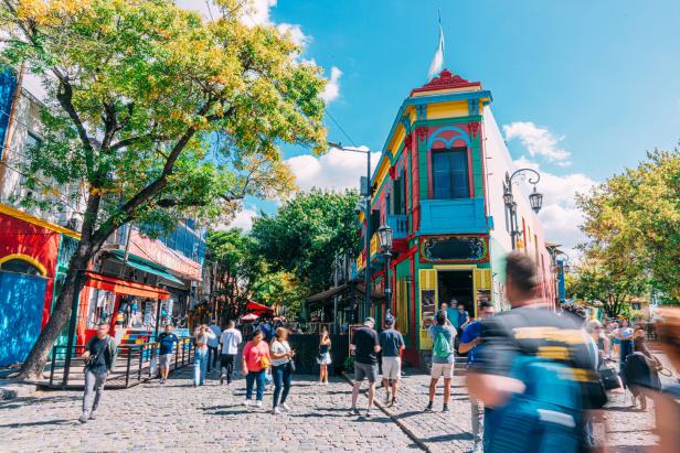 Bunte Häuser im Viertel La Boca in Buenos Aires mit vielen Passanten auf einer gepflasterten Straße unter blauem Himmel.