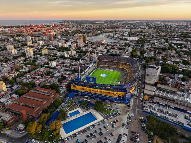 Ein großes Fußballstadion mit gelb-blauen Tribünen ist von dicht bebauten Stadtvierteln umgeben und gut besucht.