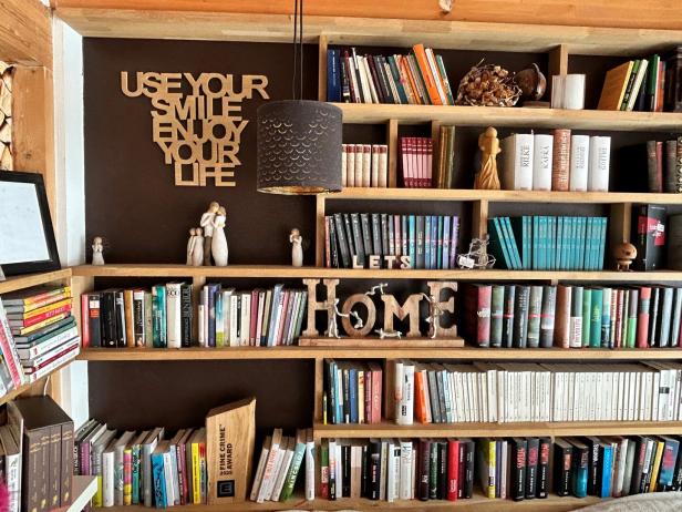 Ein Bücherregal mit vielen Büchern, Holzdeko, Figuren und dem Spruch „Use your smile, enjoy your life“ an der Wand.