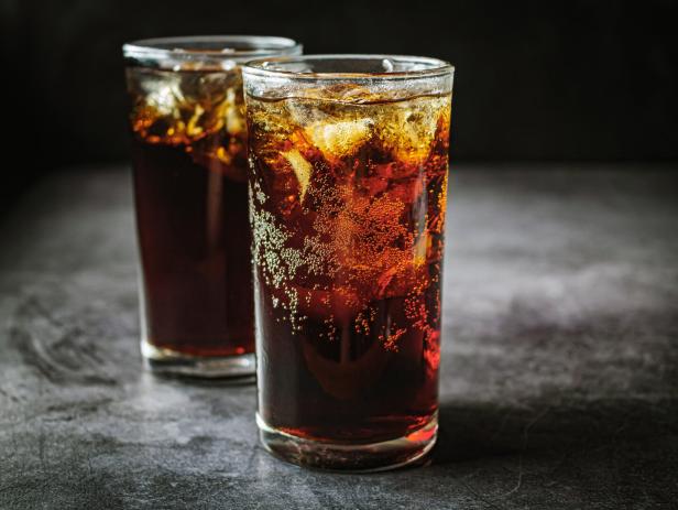 Zwei Gläser mit eiskaltem Cola und Eiswürfeln stehen auf einem dunklen Untergrund.