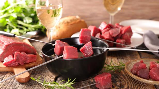 Rohe Fleischwürfel für ein Fondue mit Wein und Brot auf einem Holztisch.