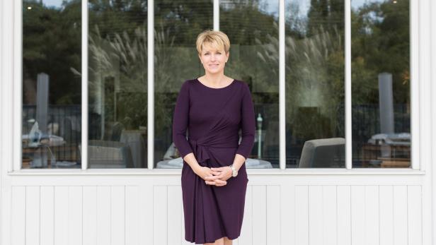 Eine Frau in einem violetten Kleid steht vor einem Fenster.