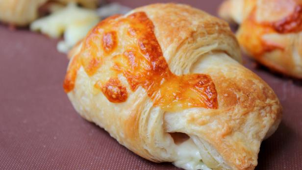 Ein Käsekipferl liegt auf einer braunen Oberfläche.