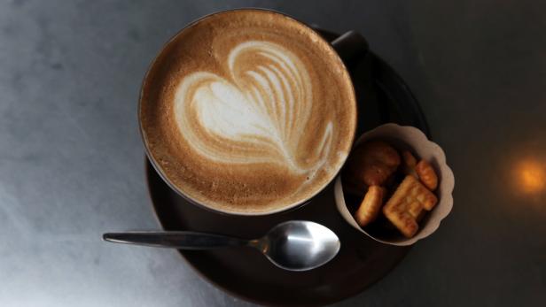 Ein Cappuccino mit Herzmuster im Milchschaum, serviert mit einer kleinen Portion Gebäck.