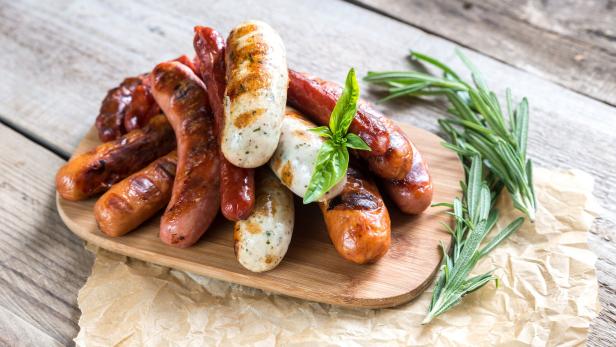 Verschiedene fertig gebratene Bratwürste auf einem Holzbrett gestapplet