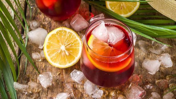 Zwei Gläser Sangria mit Eis und Zitronenscheiben auf einem Holztisch.
