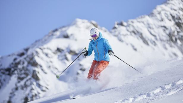 Skifahrerin wedelt über die Piste, der Schnee staubt