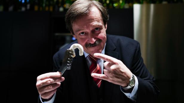 Werner Gruber präsentiert mit einer Zange das fertige Kipferl - und formt dazu mit der anderen Hand Teufelshörner (oder die Pommesgabel).