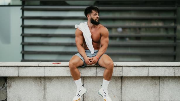 Muscular man relaxing after exercising in the city park
