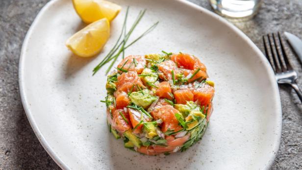 PERUVIAN FOOD. Salmon ceviche with avocado, spring onion and lemon on white plate served with white wine