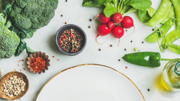 Fresh greens, vegetables and grains with white plate in center