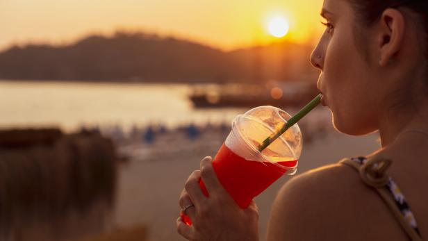 Eine junge Frau schlürft genüsslich einen Slushie im Sonnenuntergang an einem Seeufer