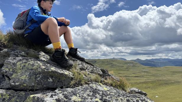 Kind sitzt auf einem Felsen und schaut in die Landschaft