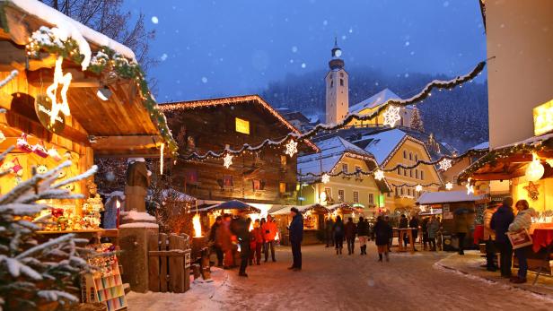 Weihnachtsmarkt mit beleuchteten Holzständen, schneebedecktem Boden und Kirche im Hintergrund bei Abenddämmerung.