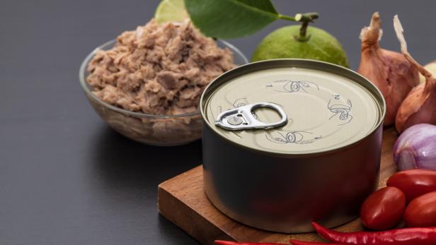 Eine ungeöffnete Konservendose steht neben einer Schale mit Thunfisch, Limette, Schalotten, Tomaten und roten Chilischoten.