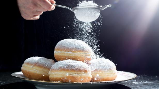 Ein Teller Krapfen wird mit Puderzucker bestreut.