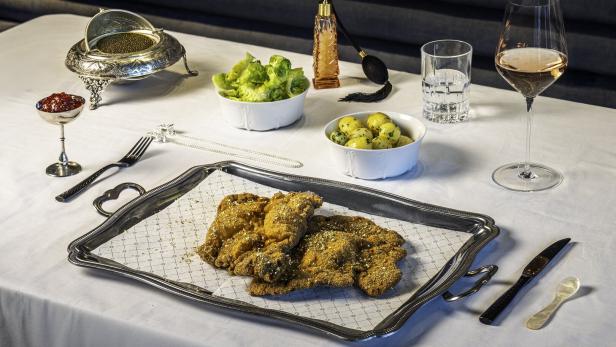 Auf einem gedeckten Tisch stehen Schnitzel auf einem Serviertablett, dazu Salat, Kartoffeln, Kaviar und Getränke.