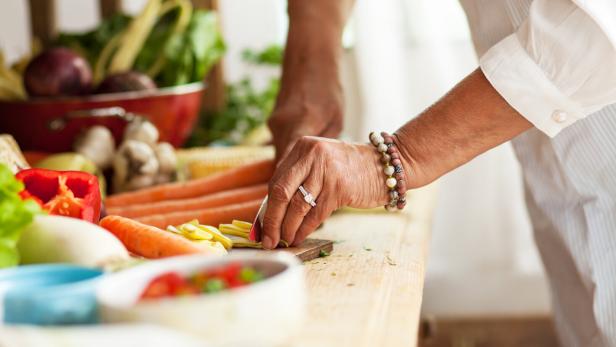 Eine Person schneidet frisches Gemüse auf einem Holztisch, umgeben von weiteren Gemüsesorten.