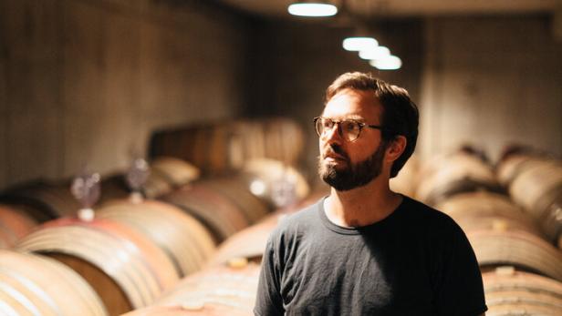 Winzer Franz Weninger steht in seinem Weinkeller zwischen Fässern