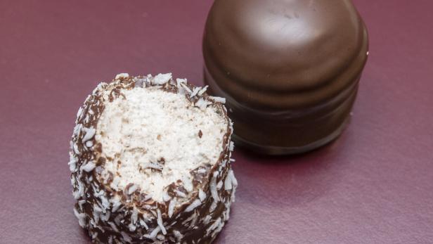 Zwei Schokoküsse, einer davon mit Kokosraspeln und angebissen, auf einer roten Oberfläche.