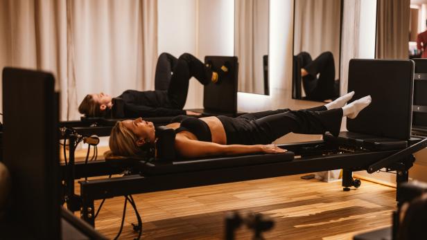 Zwei Frauen trainieren auf Pilates-Reformer-Jumpboard-Geräten in einem hellen Studio.