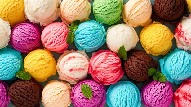 Viele bunte Eiskugeln in verschiedenen Geschmacksrichtungen, einige mit Minzblättern garniert, liegen dicht nebeneinander.
