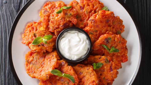Tomatokeftedes, knusprige griechische Tomatenlaibchen, angerichtet mit Joghurtdip auf einem Teller.