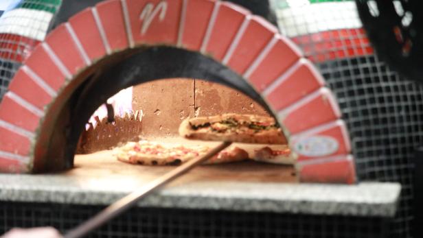 Zwei Pizzen werden mit einer Schaufel in einem traditionellen Steinofen gebacken.