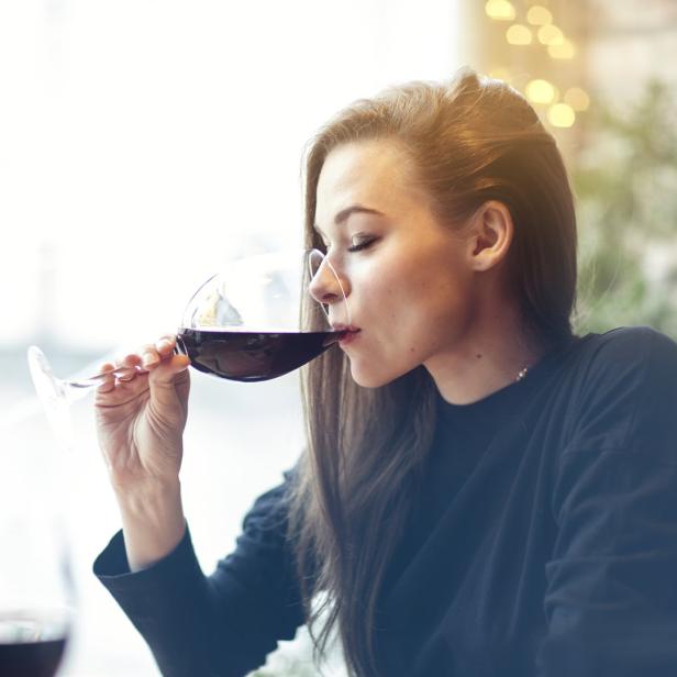 Frau trinkt Rotwein aus langstieligem Glas