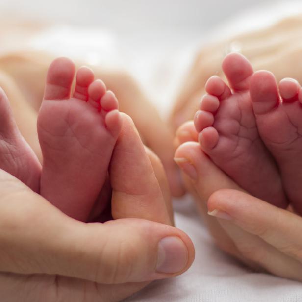 Mother and father's hands cradling twin babies' feet on a pale background