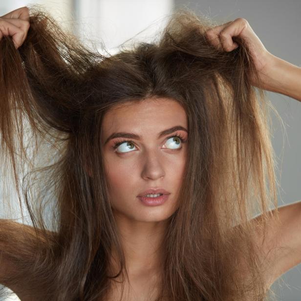 Eine junge Frau hält ihr trockenes, braunes Haar hoch und blickt nach oben.