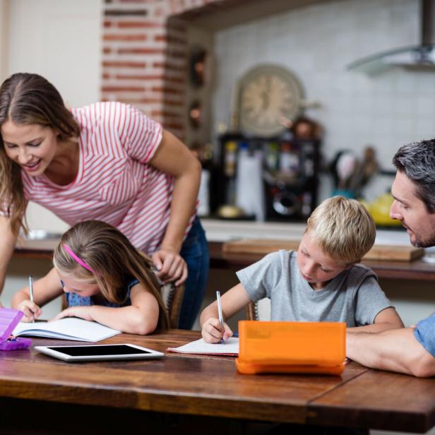 Vater, Mutter und ihre beiden Schulkinder beim Hausaufgaben machen