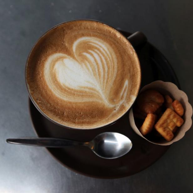 Ein Cappuccino mit Herzmuster im Milchschaum, serviert mit einer kleinen Portion Gebäck.
