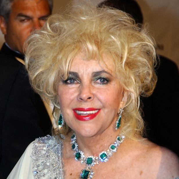 Elizabeth Taylor mit blonden Locken, smaragdgrüner Halskette und passenden Ohrringen lächelt.