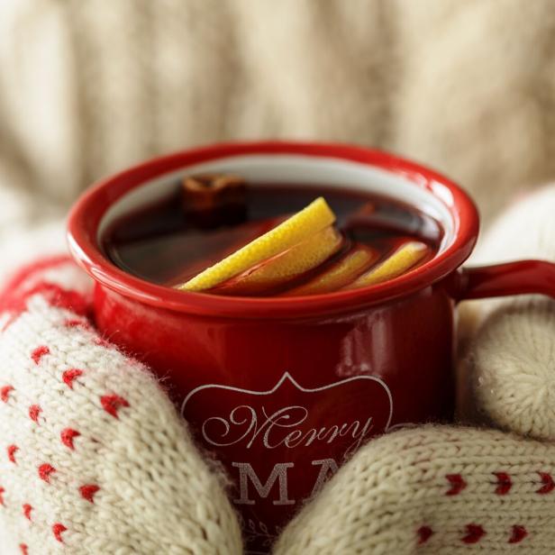 Hände in Fäustlingen halten eine volle Tasse Glühwein