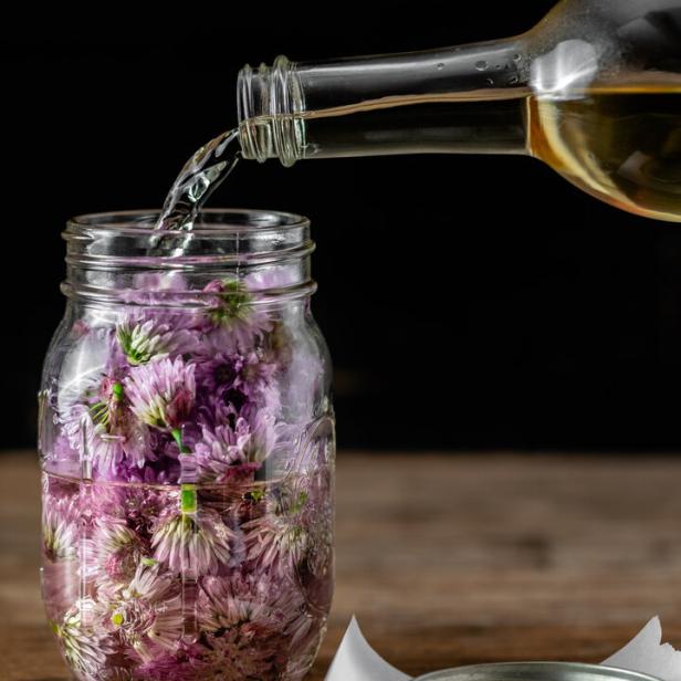 Wine vinegar being poured into a canning jar full of chives blossoms