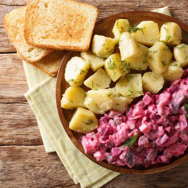 Tasty herring salad with vegetables and a side dish of boiled potatoes close-up in a plate. Horizontal top view