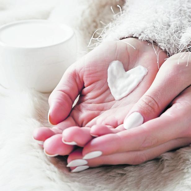 Beautiful groomed woman's hands with cream jar on the fluffy blanket. Moisturizing cream for clean and soft skin in winter time. Heart shape created from cream. Love a body. Healthcare concept.