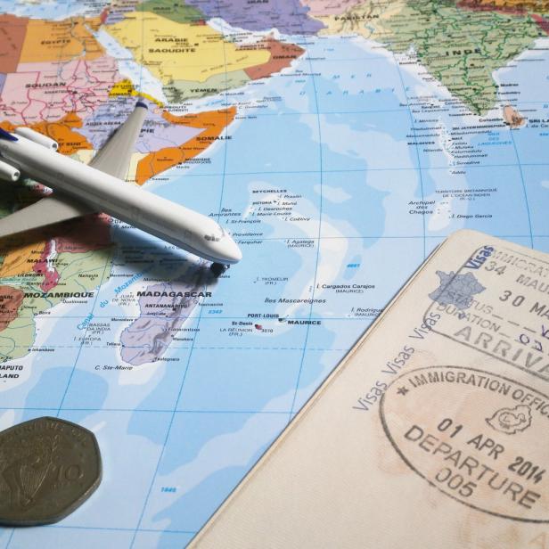 Ein Spielzeugflugzeug steht auf einer Weltkarte neben einem Reisepass mit einem mauritischen Einreisestempel.